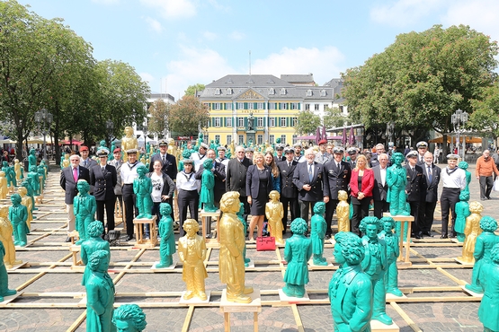 Die Mitglieder des FK-EGV Bonn, auf dem Bonner Münsterplatz. Im Vordergrund sind die ikonischen grünen und goldenen Beethoven-Figuren zu sehen. Im Hintergrund steht die alte Bonner Post.